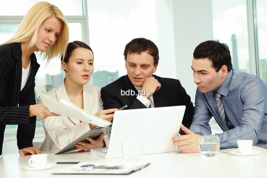 Фотография группы людей за столом, обсуждающих изображение на экране ноутбука